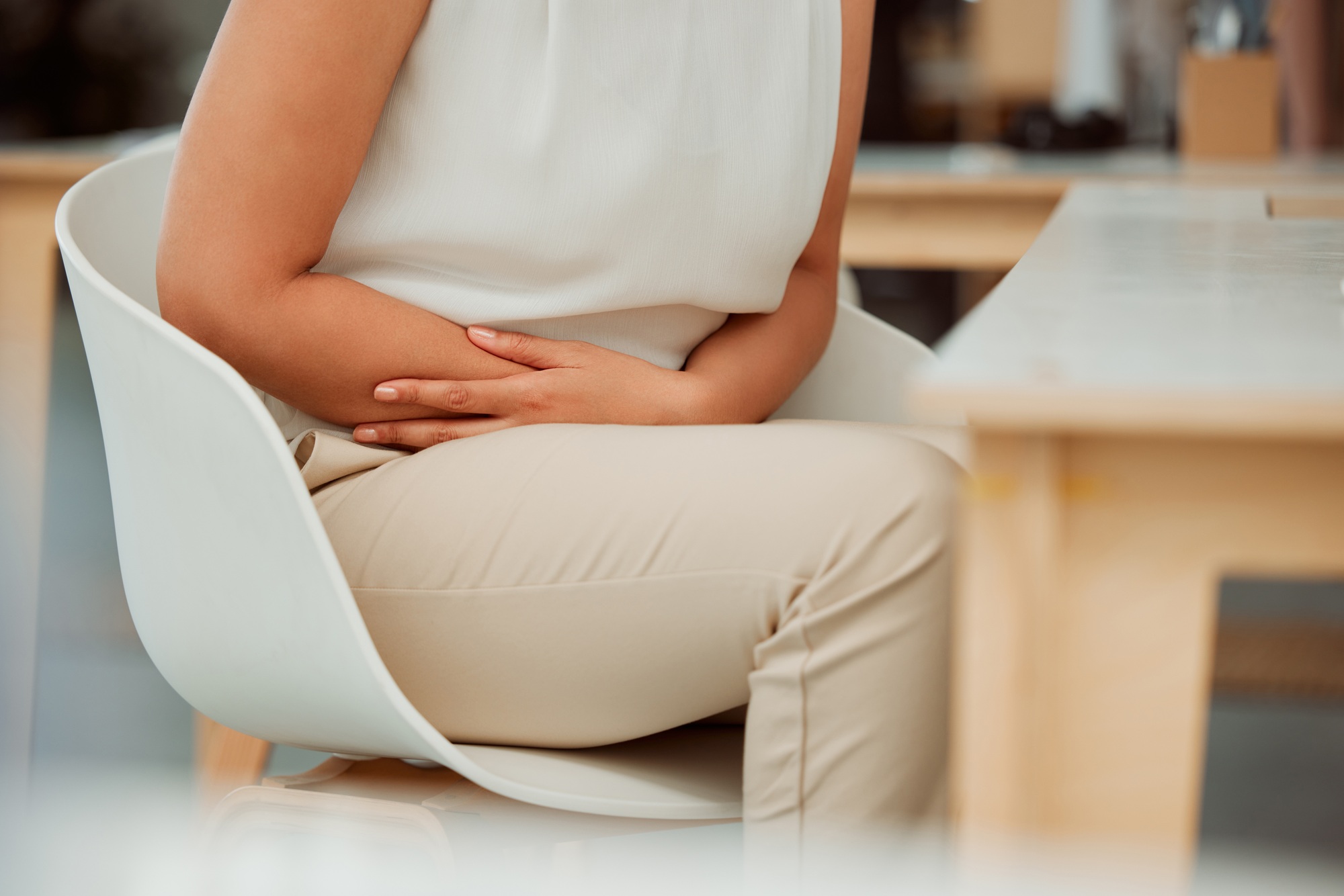 Closeup of one mixed race business woman holding sore tummy while feeling ill with menstrual stomac